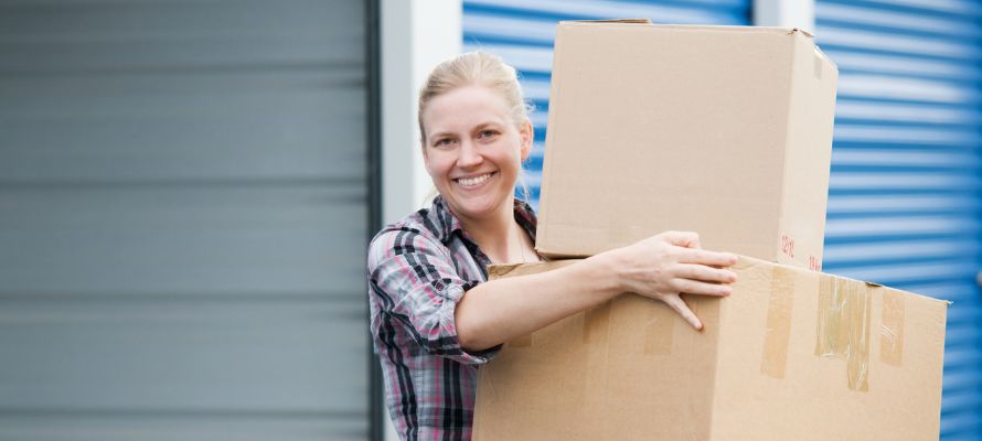 Smiling woman carrying cardboard boxes in front of self-storage units